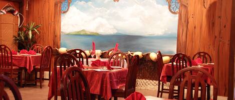 A restaurant with wooden walls, red tablecloths, and a mural of a coastal landscape.
