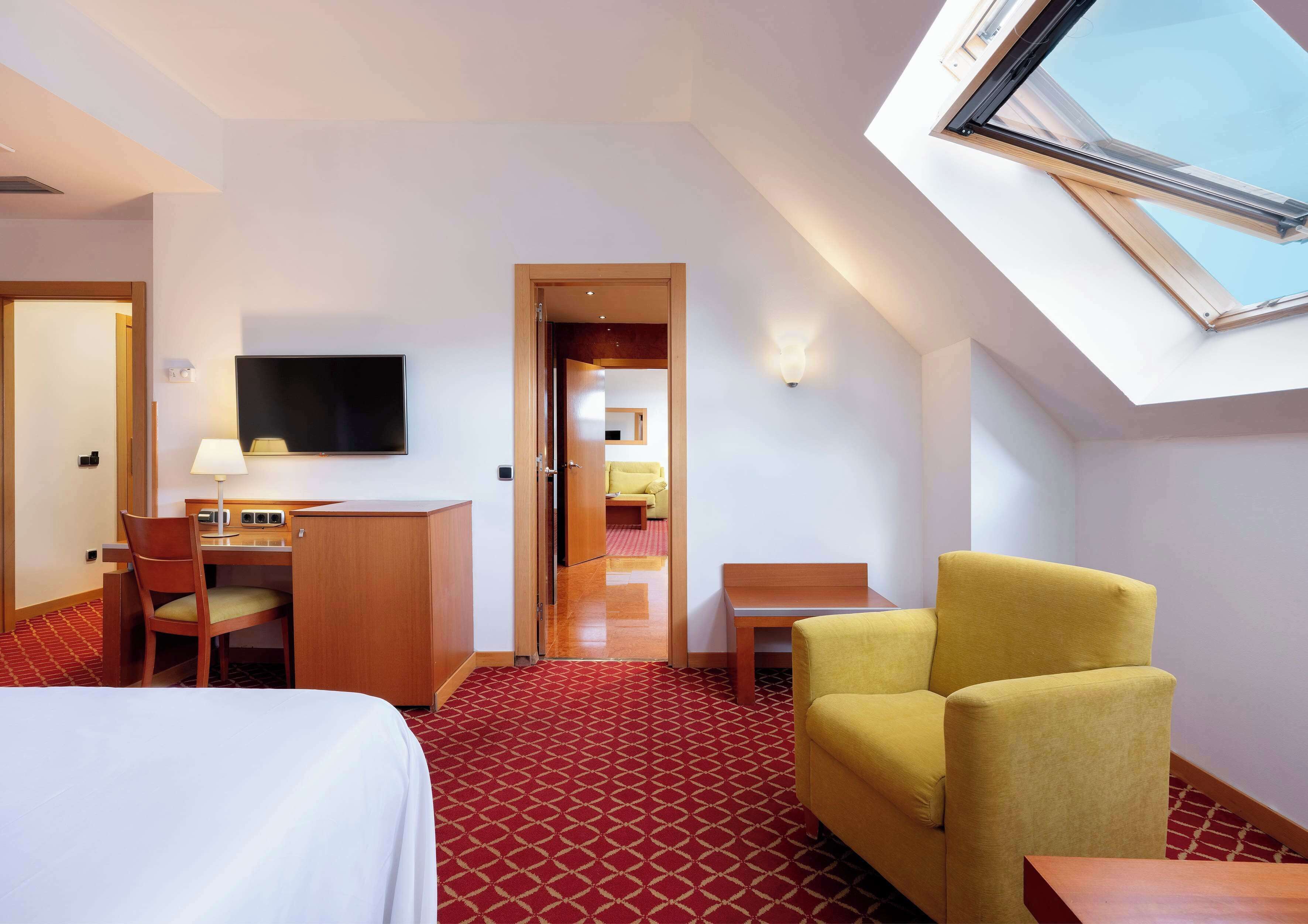 Ein Hotelzimmer mit einem Bett, einem Schreibtisch, einem Stuhl, einem Fernseher und einem Oberlicht.