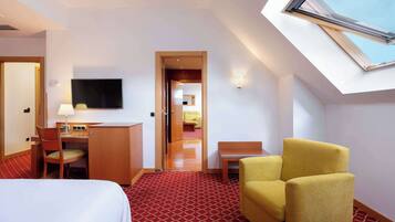 Habitación de hotel con cama, escritorio, silla, televisor y tragaluz.