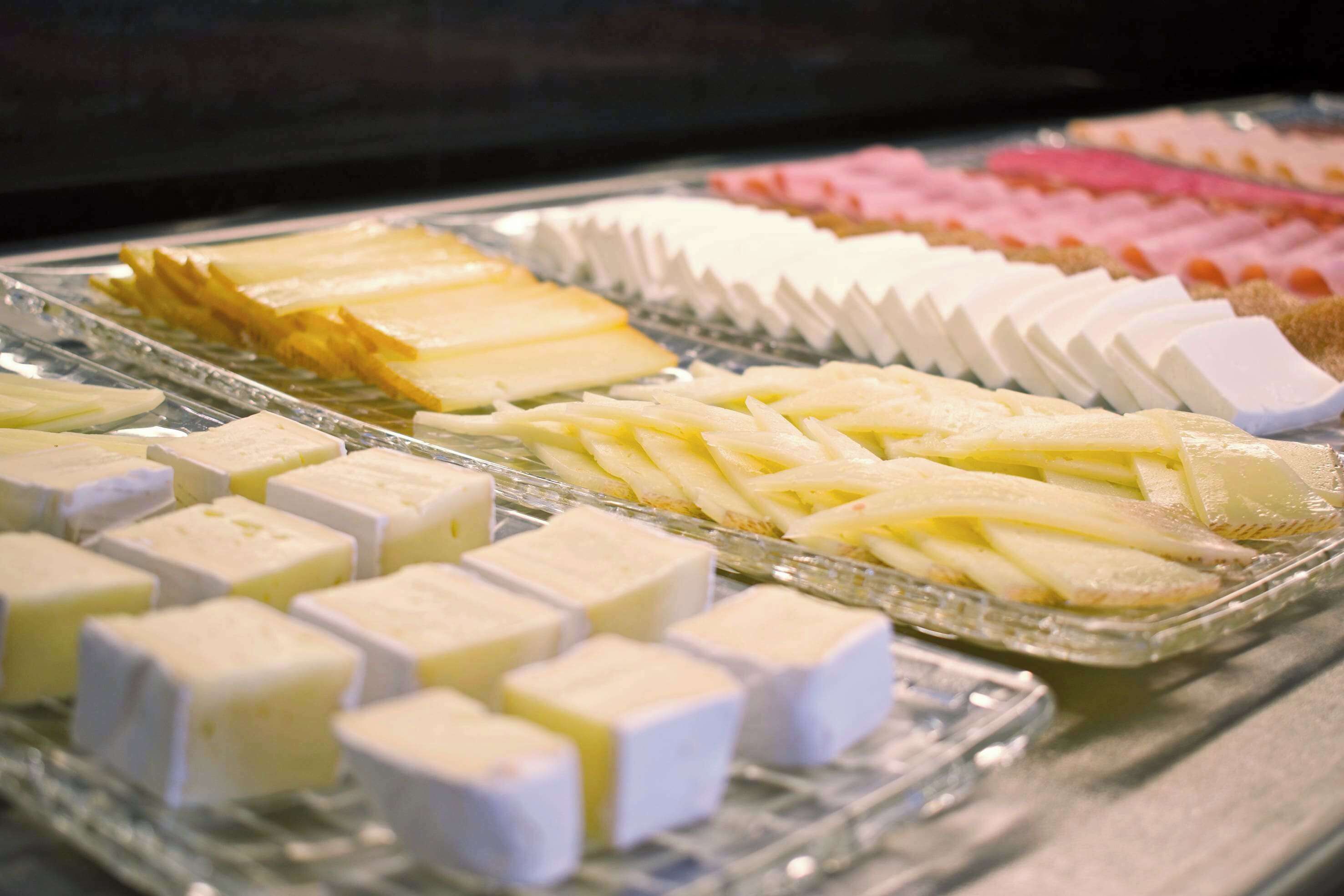 A display of various cheeses and cured meats in a glass case.