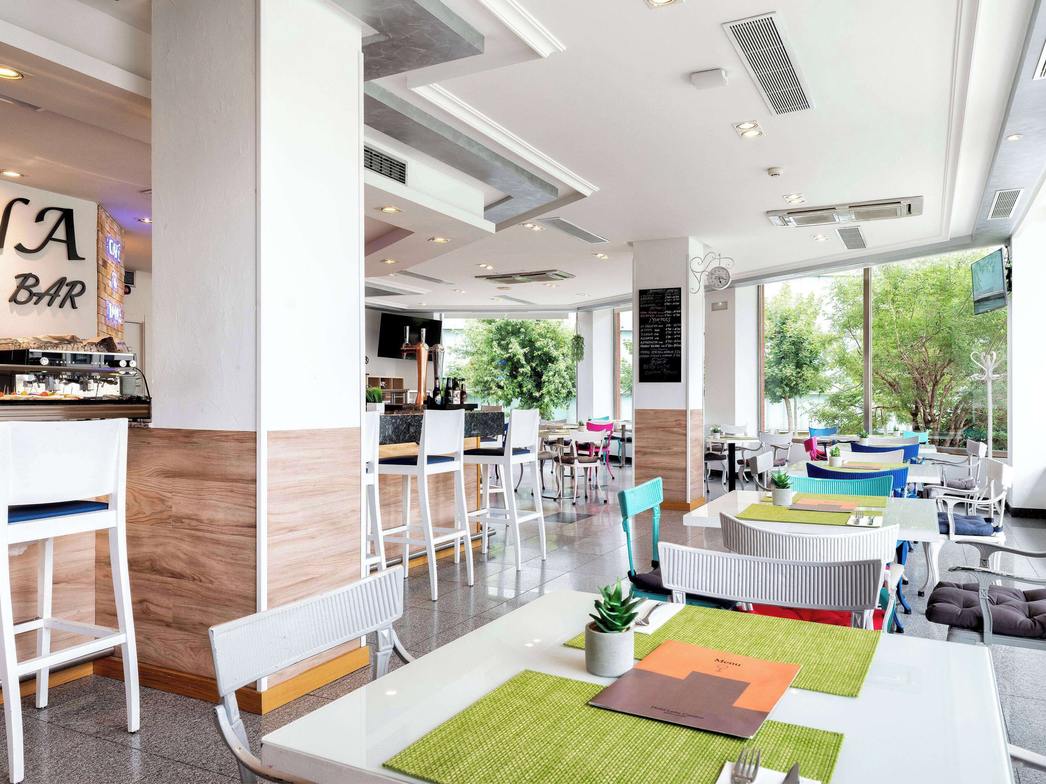 A modern bar area with a bar counter, seating, and a large window offering a view of greenery outside.