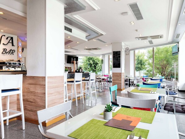 A modern bar area with a bar counter, seating, and a large window offering a view of greenery outside.