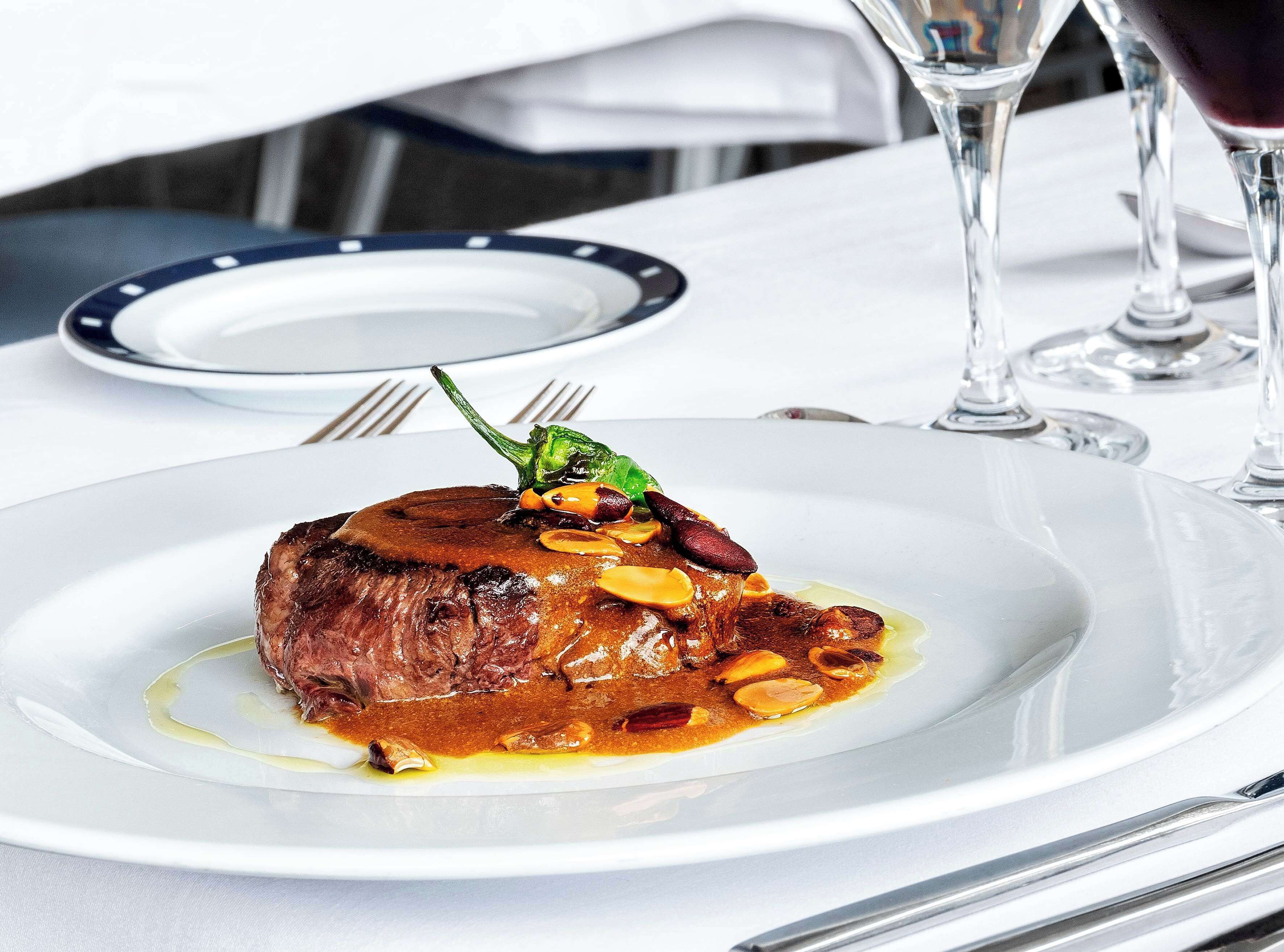 A plate of steak with a garnish of herbs and nuts, accompanied by a glass of red wine.