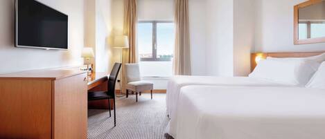 A hotel room with a bed, a desk, a chair, a TV, and a window with curtains.