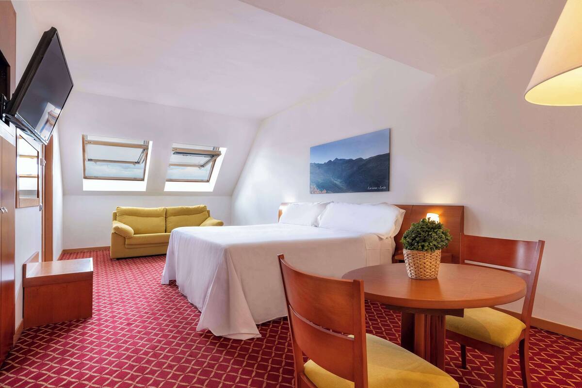 A hotel room with a bed, a sofa, a dining table, and a TV.