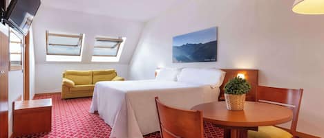 Ein Hotelzimmer mit Bett, Sofa, Esstisch und Fernseher.
