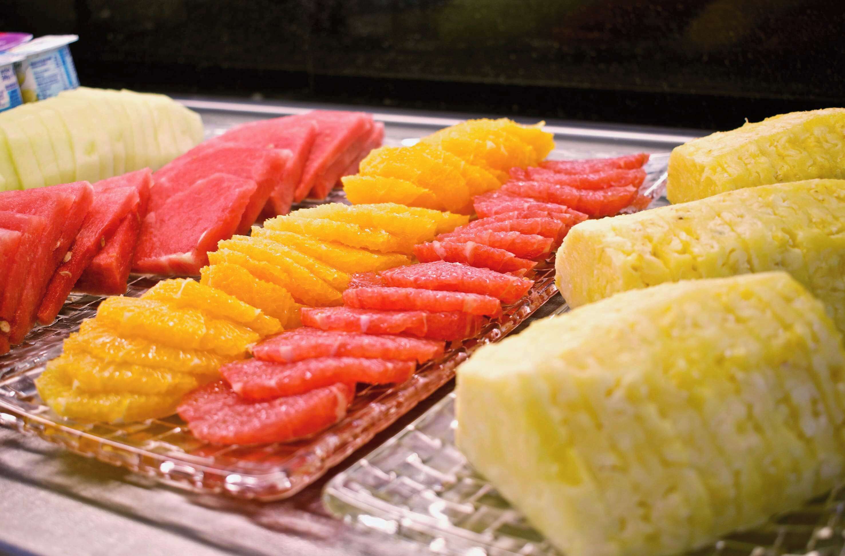A selection of fresh fruits including watermelon, orange, and corn on a glass tray.