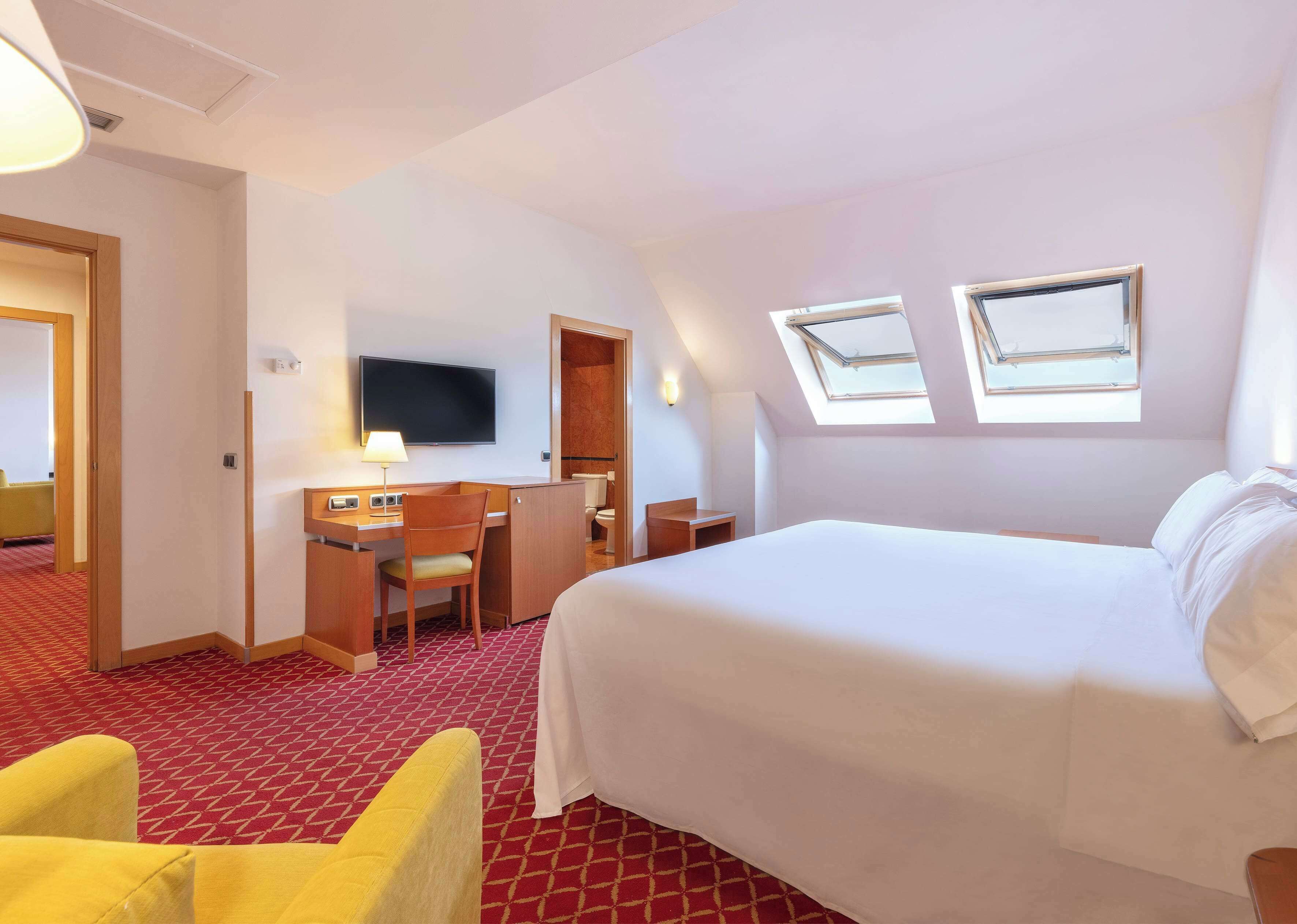 Una habitación de hotel con cama, escritorio, silla y televisor.