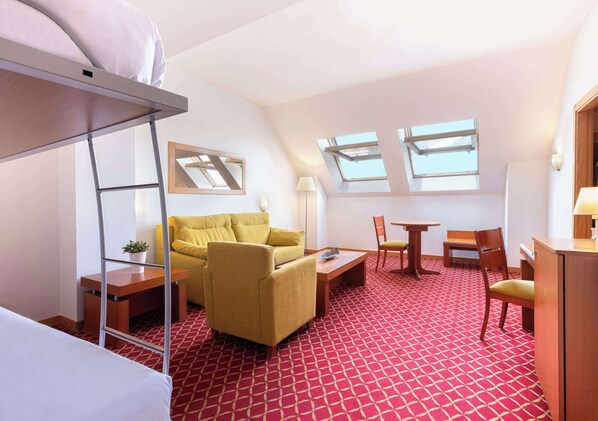 A hotel room with a bunk bed, a yellow sofa, a small table, a chair, a desk, and a red patterned carpet. - Hotel Zentral Leon Camino (León)