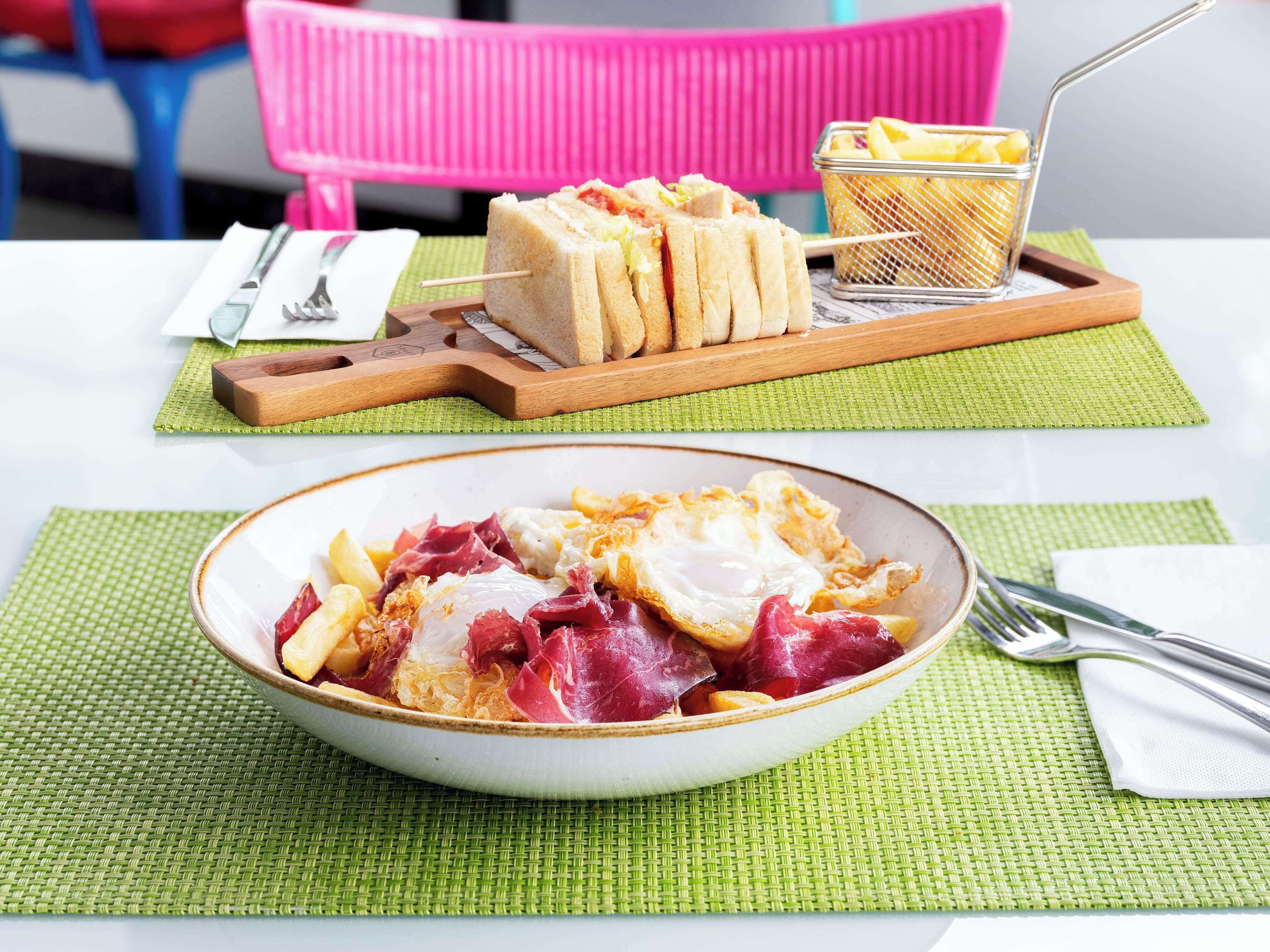 A meal with sandwiches and a bowl of eggs and ham on a table with a green placemat.