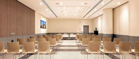 Een vergaderzaal met rijen stoelen, een marmeren vloer en een hoog plafond met inbouwverlichting.