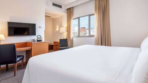 A hotel room with a large bed, a desk with a chair, a television, and a window with curtains.
