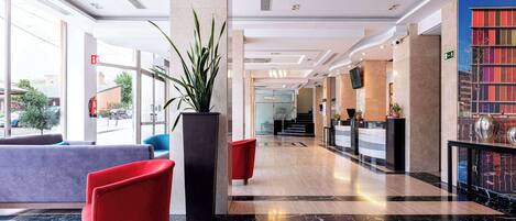 A modern lobby with a reception desk, seating area, and a large plant.