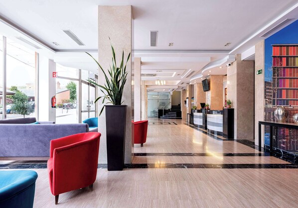 A modern lobby with a reception desk, seating area, and a large plant.