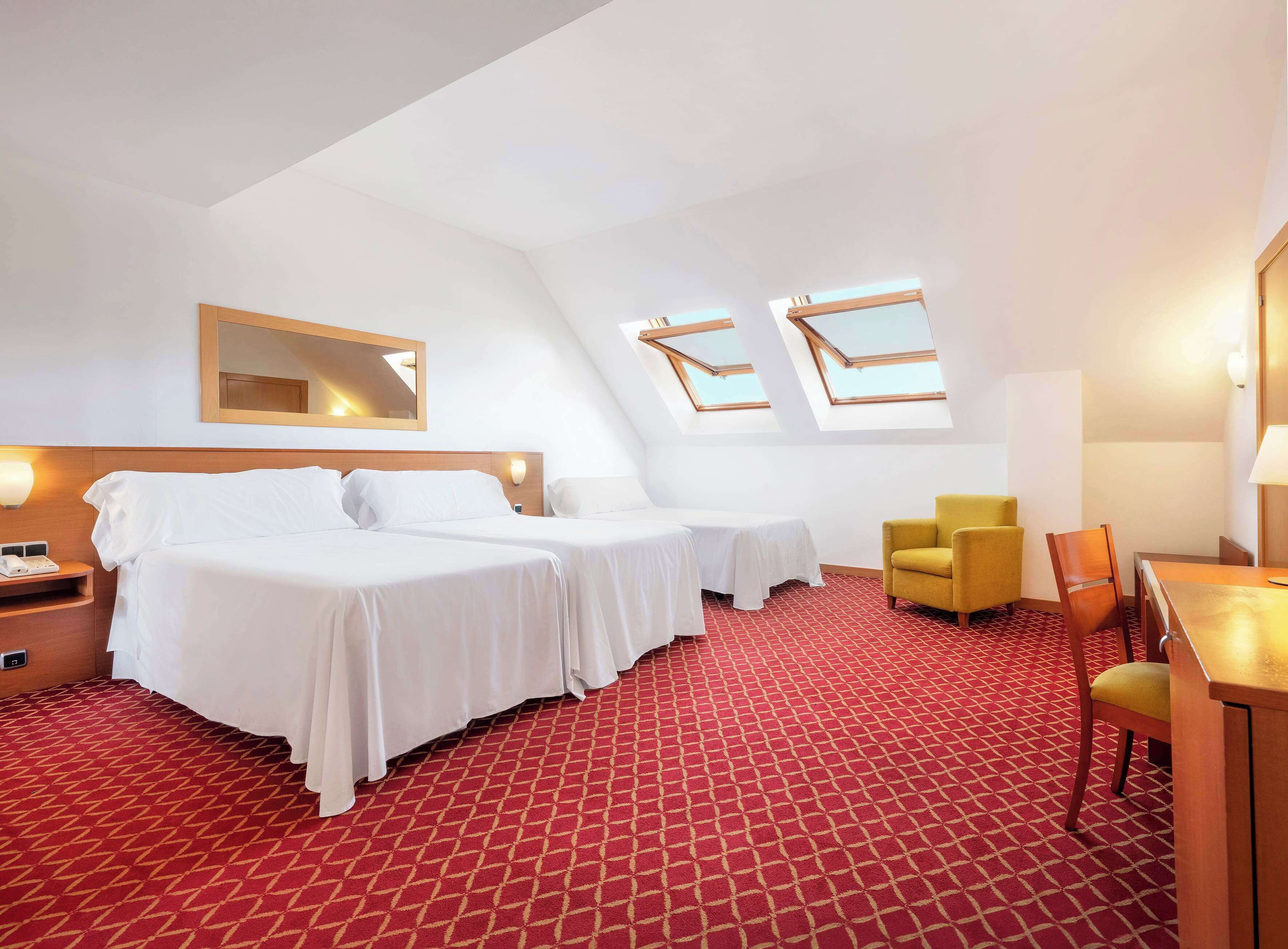 A hotel room with two beds, a desk, a chair, and a red patterned carpet.