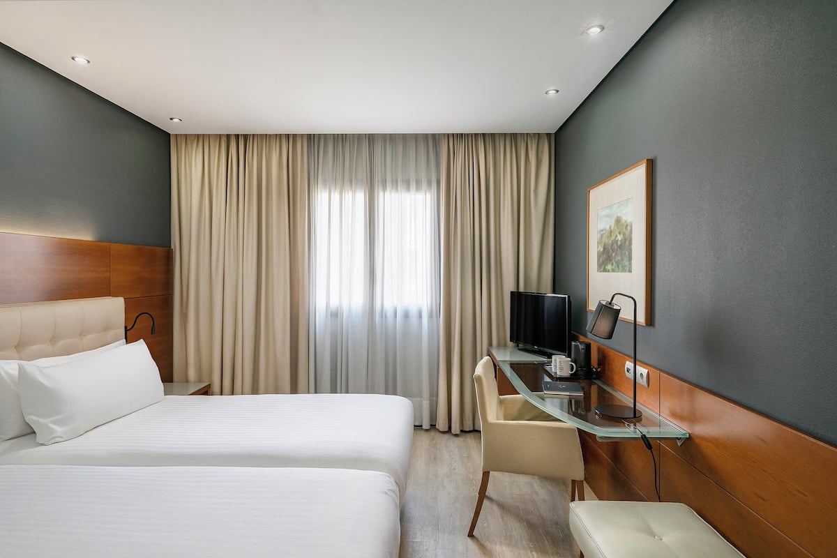 A hotel room with two beds, a desk with a flat-screen TV, a coffee maker, and a framed picture on the wall.