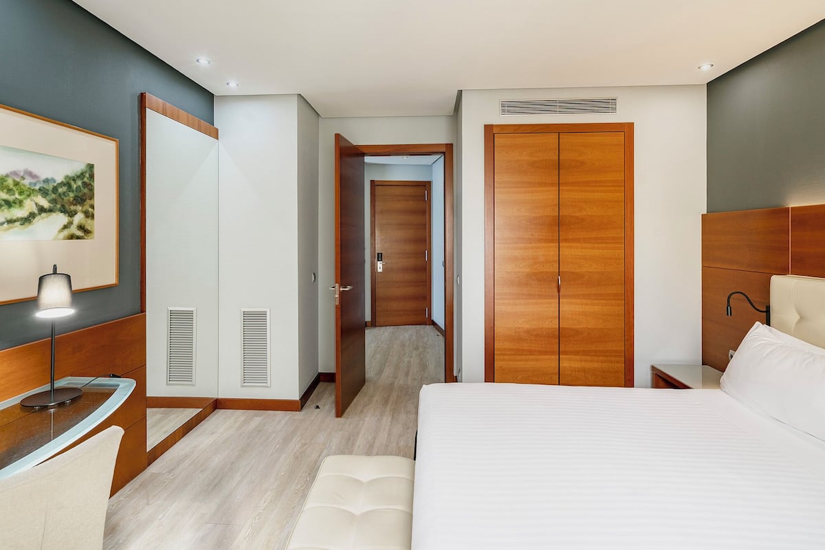 A hotel room with a bed, bedside table, lamp, and a large wooden wardrobe.