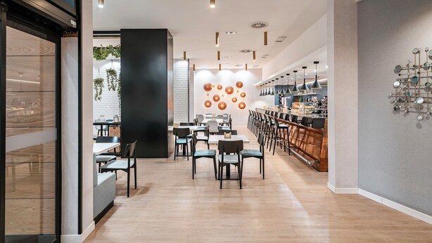 Et moderne interiør med et centralt siddeområde, en bar til højre og et køkken, der ses gennem en glasvæg.