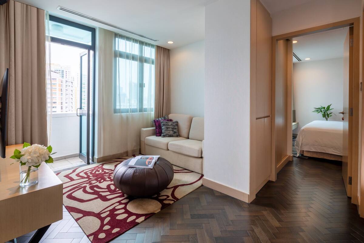 A modern hotel room with a sofa, ottoman, and a bed.