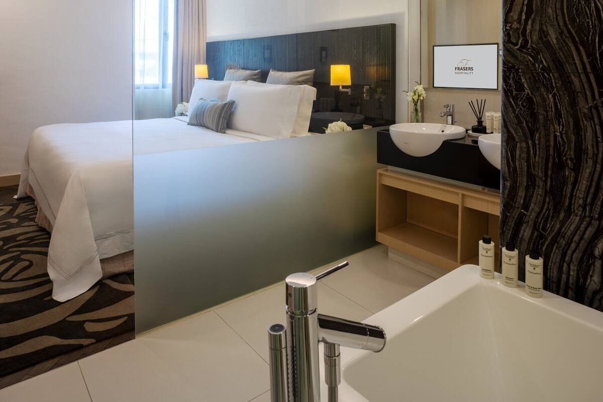 A modern hotel room with a large bed, a separate bathroom with a bathtub, and a large mirror.