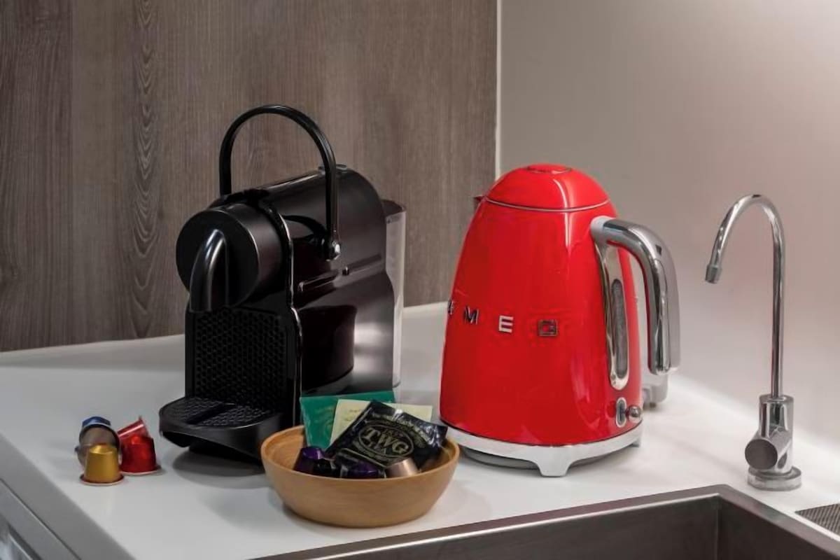 A kitchen counter with a black coffee maker, a red electric kettle, a bowl of snacks, and a faucet.