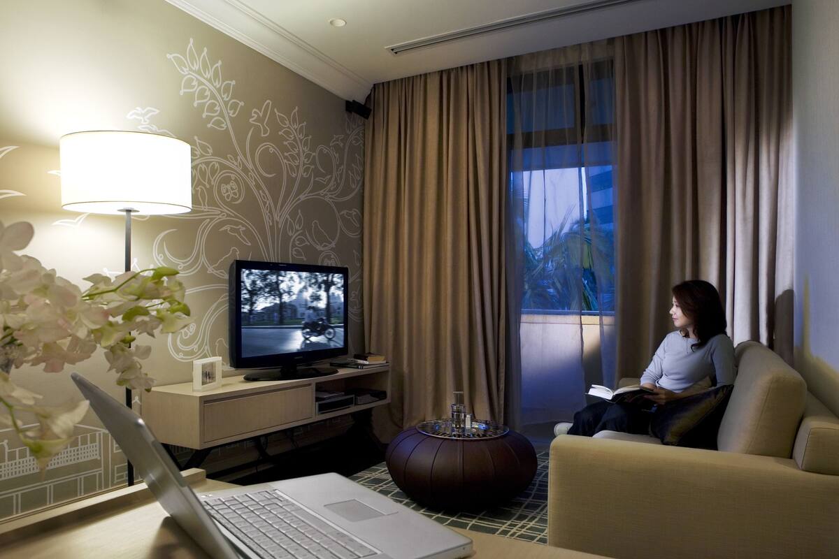 A hotel room with a laptop on a desk, a television, a sofa, and a decorative wall.