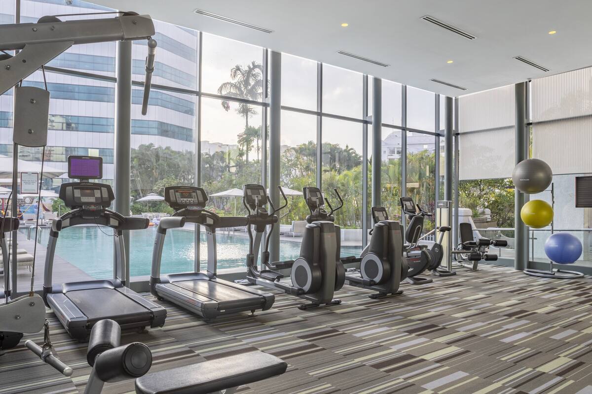 A gym with treadmills, elliptical machines, and exercise balls, overlooking a pool.
