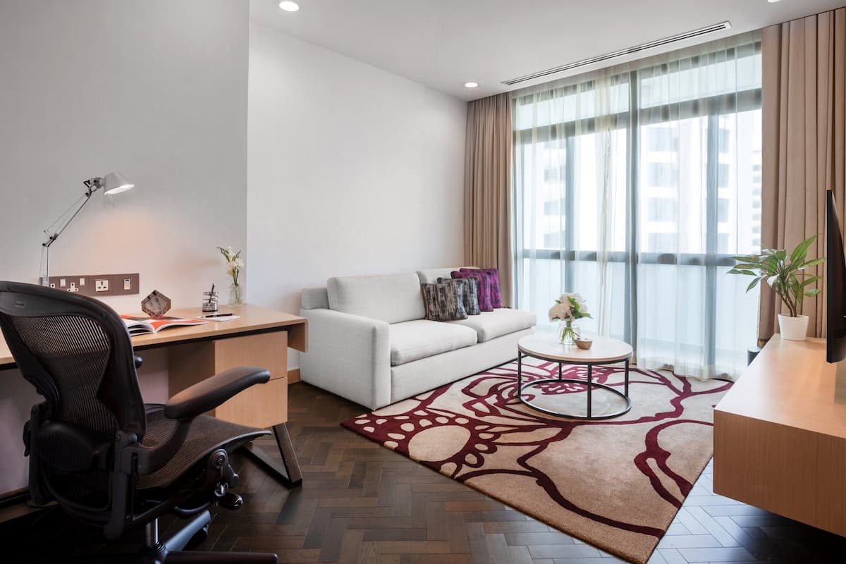 A modern office space with a desk, chair, sofa, and a large window with curtains.
