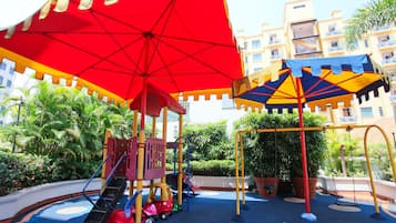 Children can play and explore in this shaded play area surrounded by lush greenery and potted plants.
