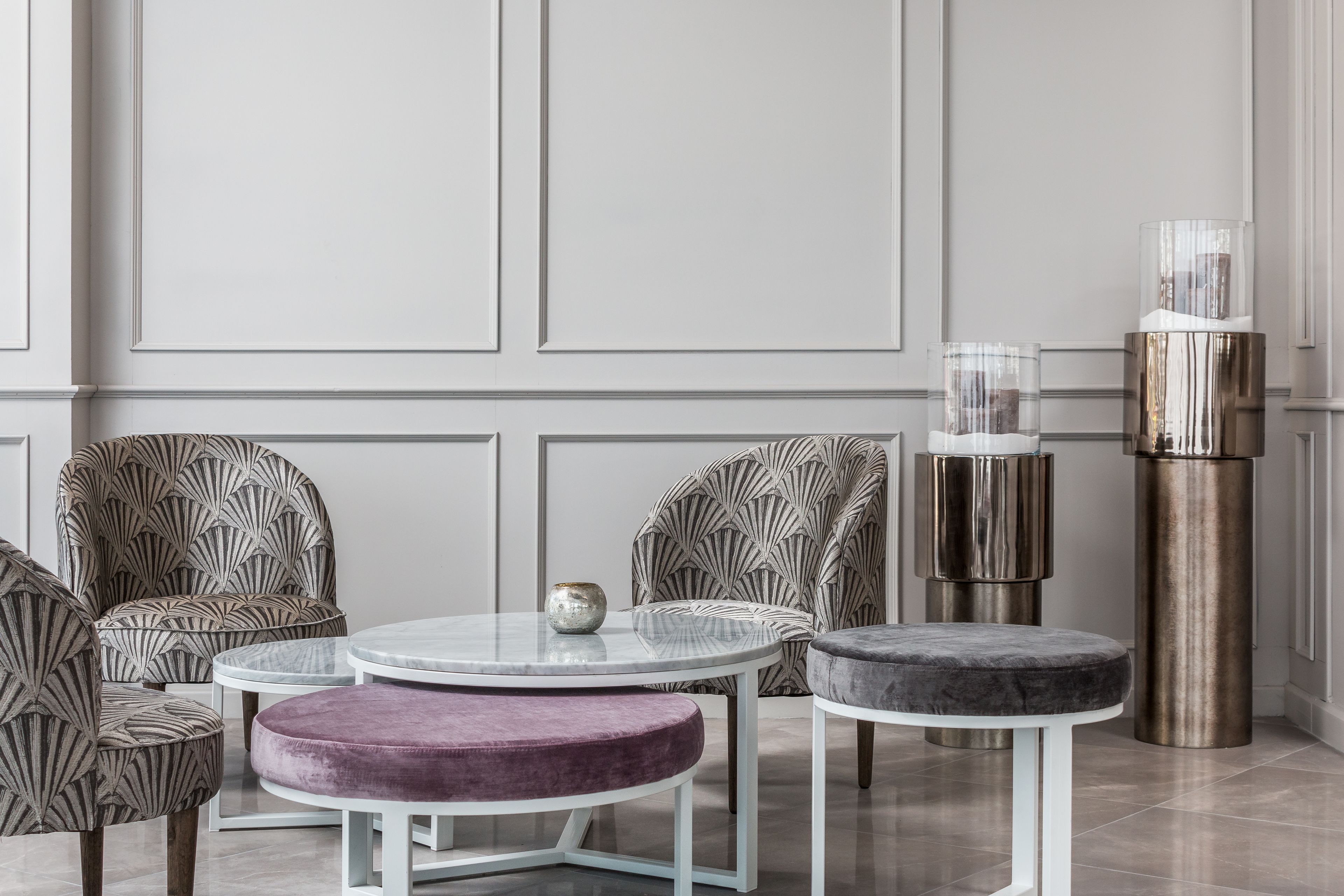 A modern interior with patterned armchairs, a round glass table, a purple ottoman, and a tall metallic column.