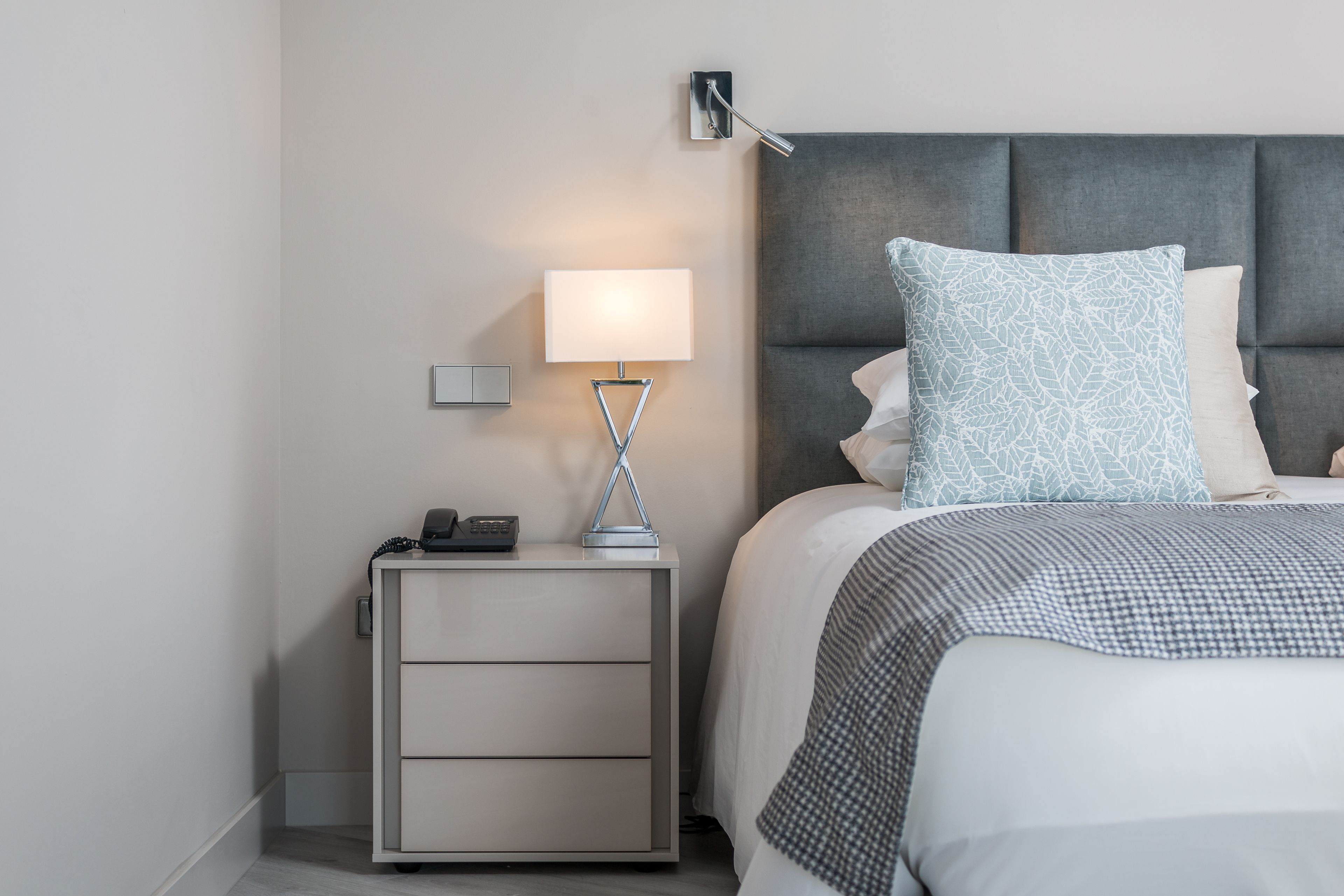 A neatly arranged bedroom with a bed, bedside table, lamp, and a wall-mounted light fixture.