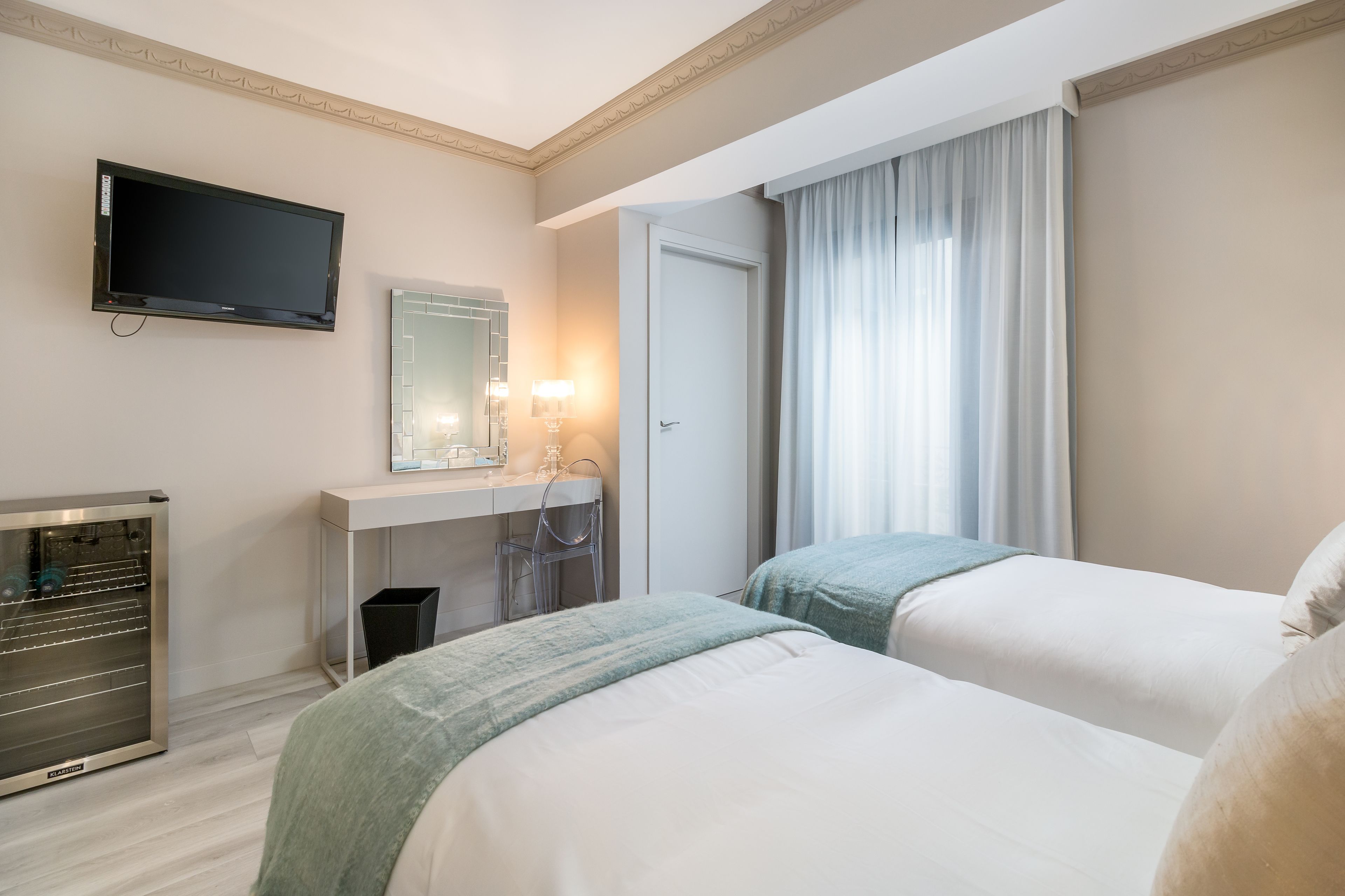 Una habitación de hotel con dos camas, televisión, escritorio con espejo y minibar.