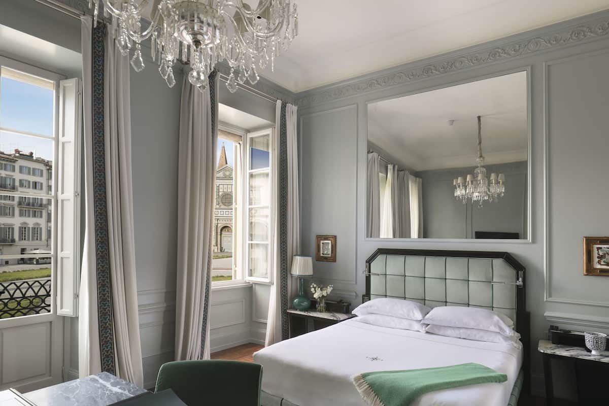 Habitación de hotel con cama, candelabro, un espejo grande y vistas a un edificio.