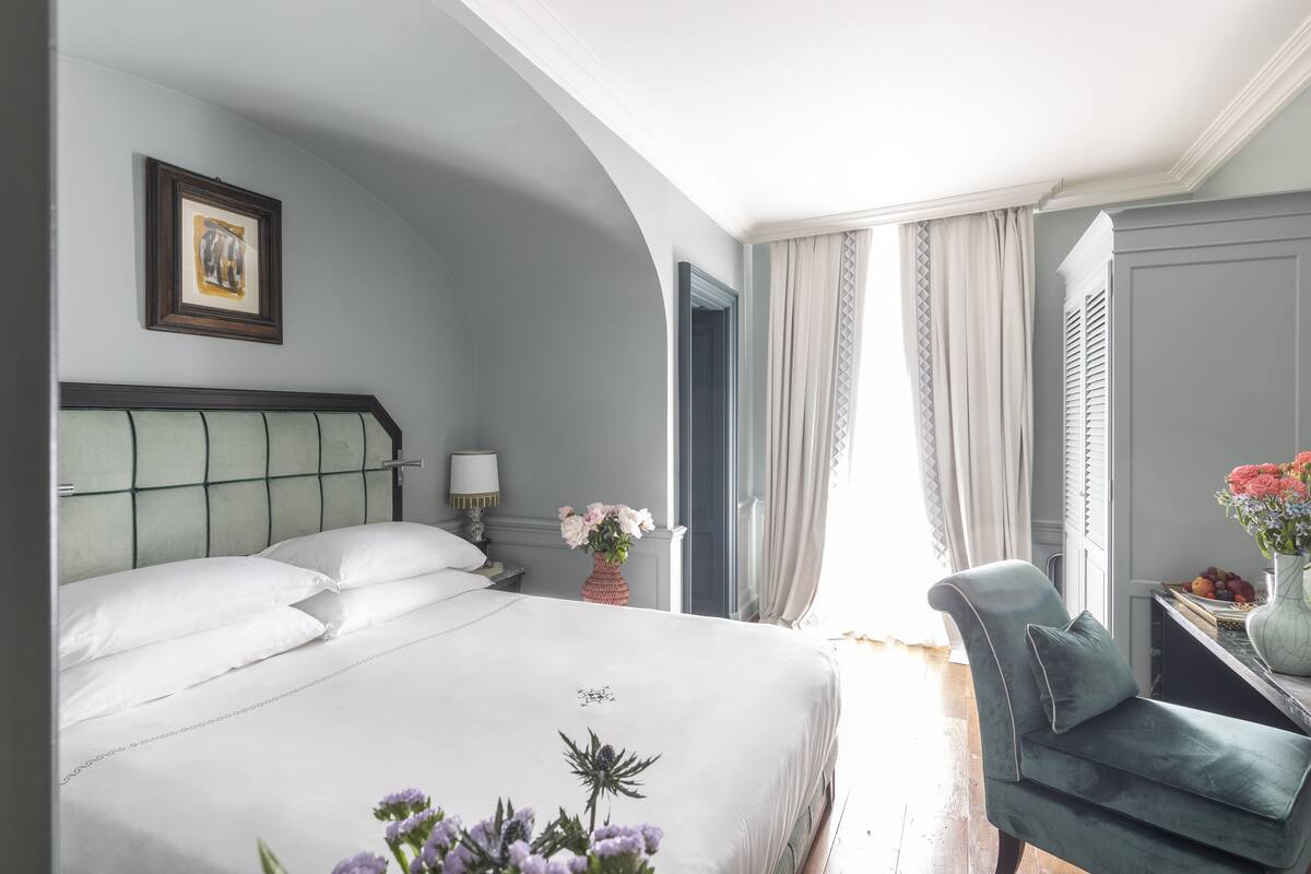 Habitación de hotel con una cama grande, una silla, un escritorio con un florero y un cuadro en la pared.