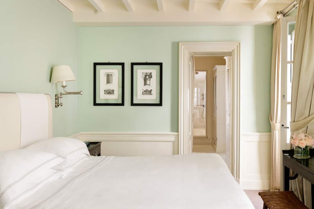 Un dormitorio con cama, mesita de noche, lámpara y dos cuadros en la pared.