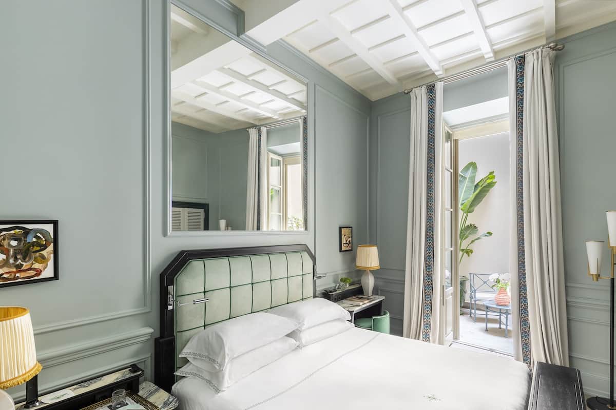 Habitación de hotel con una cama grande, una mesita de noche, una lámpara, un espejo y vistas al exterior.