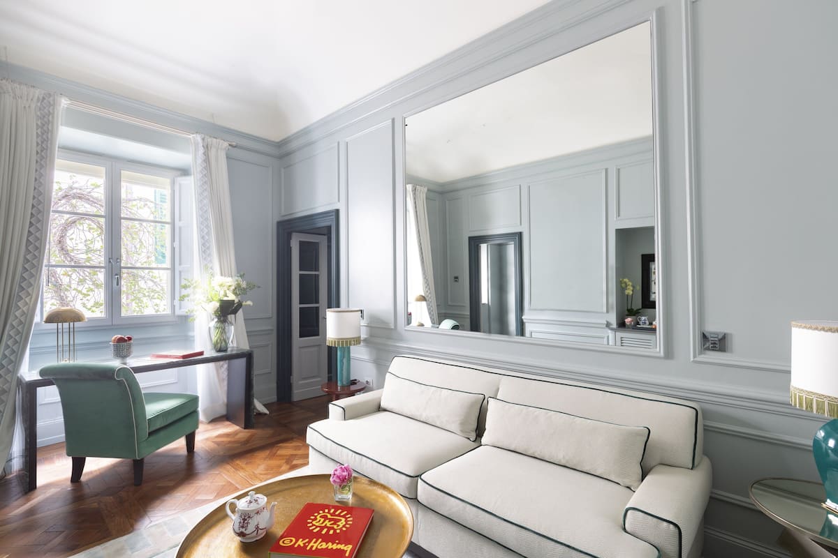Una sala de estar con un sofá, una silla, una mesa de centro con un libro, una lámpara y un espejo grande.