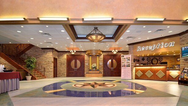 A hotel reception area with a central chandelier, a reception desk, and a staircase leading to another floor. - Baymont by Wyndham Pompton Plains/Wayne (Pompton Plains)