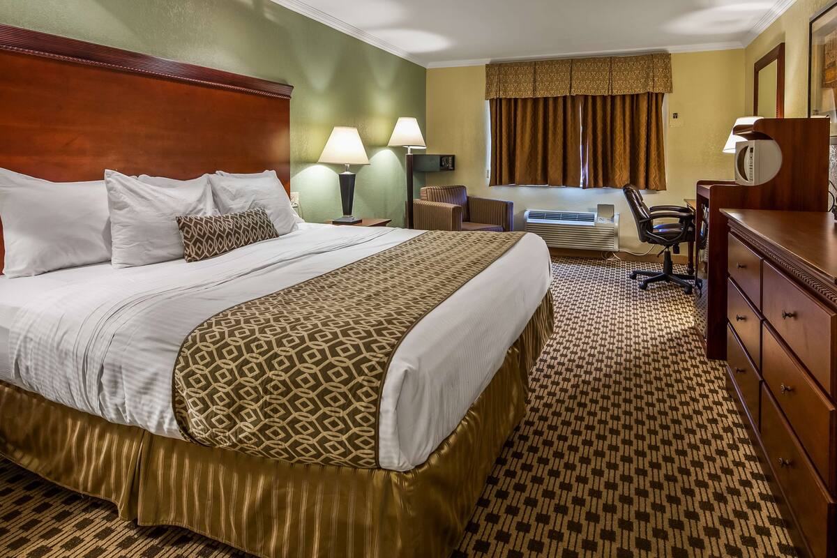 Une chambre d’hôtel avec un grand lit, deux lampes de chevet, un bureau avec une chaise, une commode et une fenêtre avec des rideaux.