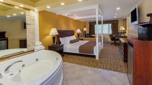 A hotel room with a large bathtub, a four-poster bed, a desk with a chair, and a television. - Baymont by Wyndham Pompton Plains/Wayne (Pompton Plains)