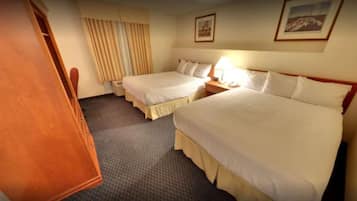 A hotel room with two beds, a wooden wardrobe, a nightstand with a lamp, and a window with curtains.