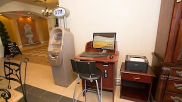 Un cajero automático, una computadora con monitor, una impresora y una silla en un área de recepción.