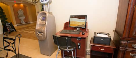Un distributeur automatique de billets, un ordinateur avec un écran, une imprimante et une chaise, le tout situé dans un espace d’accueil.