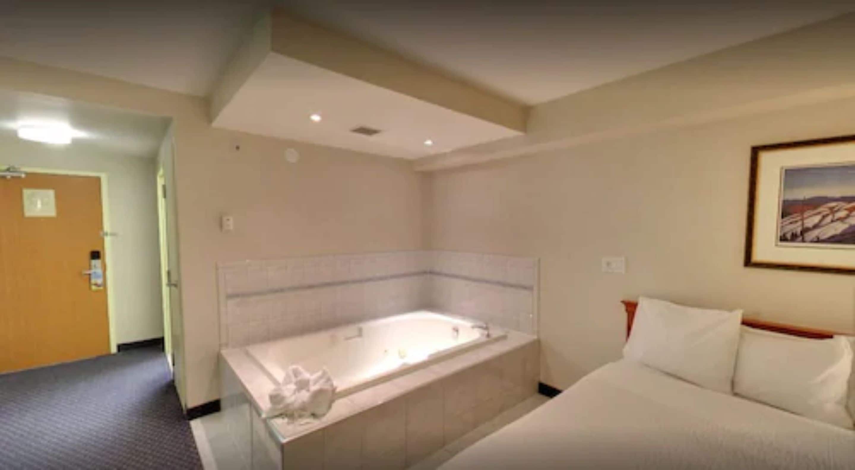 Quarto de hotel com uma banheira grande, uma cama e um quadro na parede.