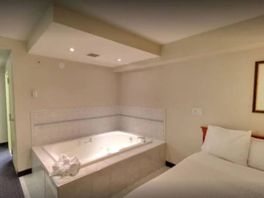 Quarto de hotel com uma banheira grande, uma cama e um quadro na parede.