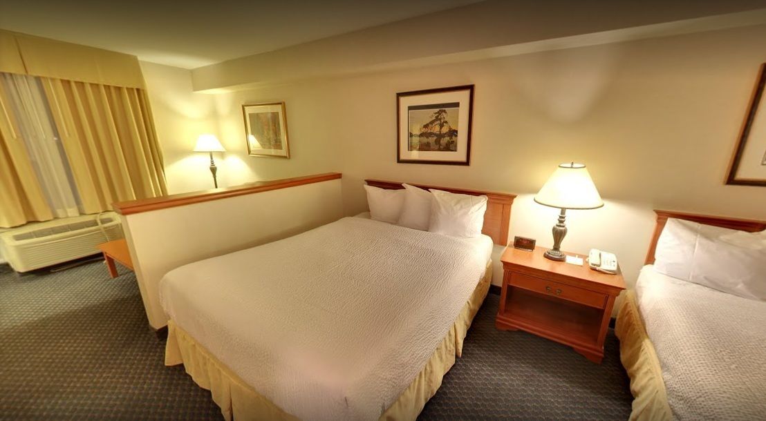 A hotel room with two beds, a bedside table with a lamp, a framed picture on the wall, and a window with curtains.