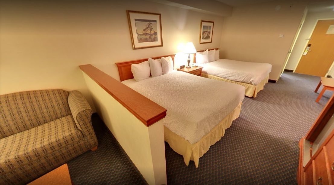 A hotel room with two beds, a sofa, a desk, and a lamp.