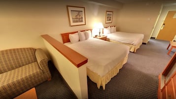A hotel room with two beds, a sofa, a desk, and a lamp.