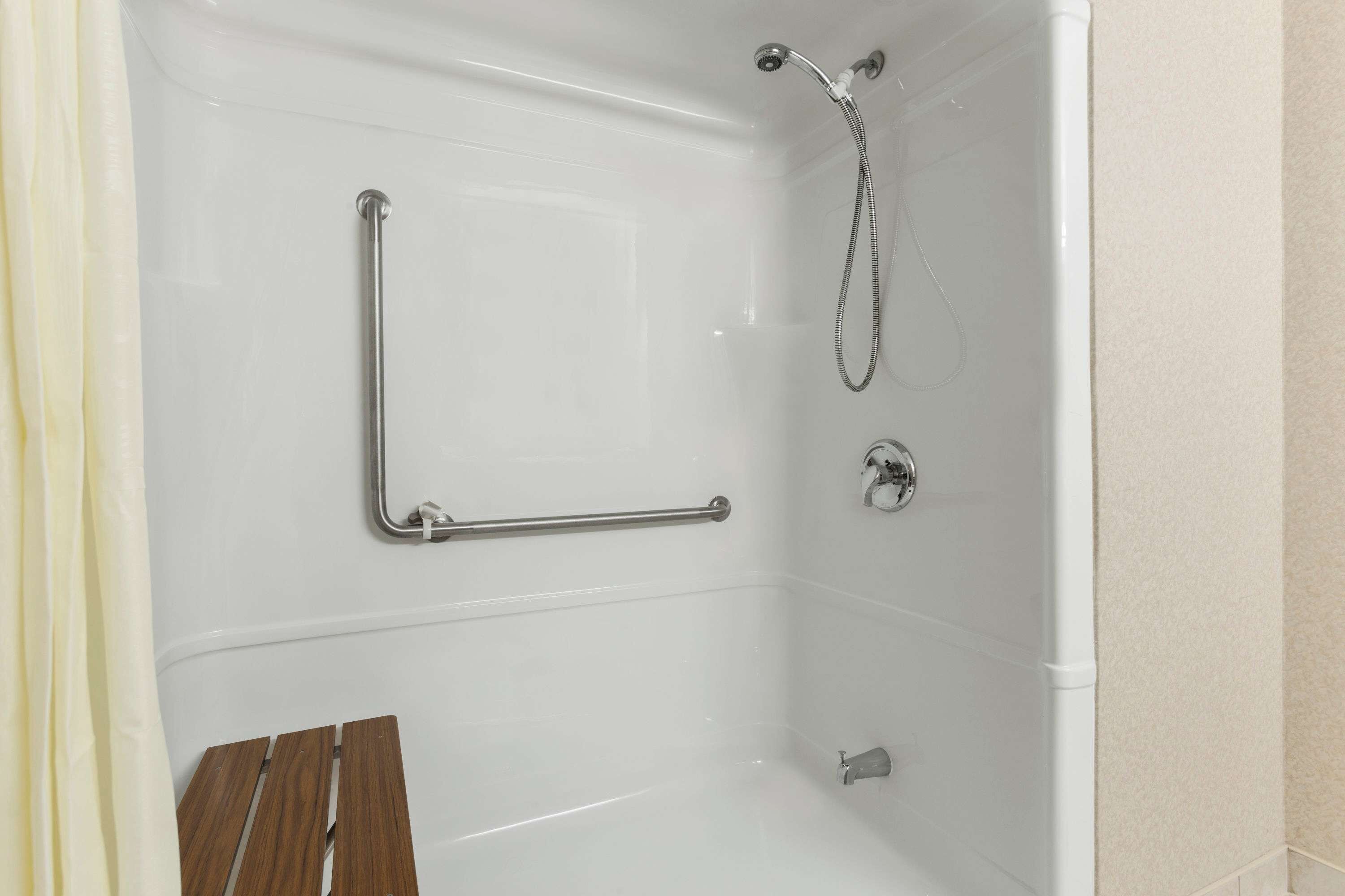 A white bathtub with a handheld showerhead and a grab bar.