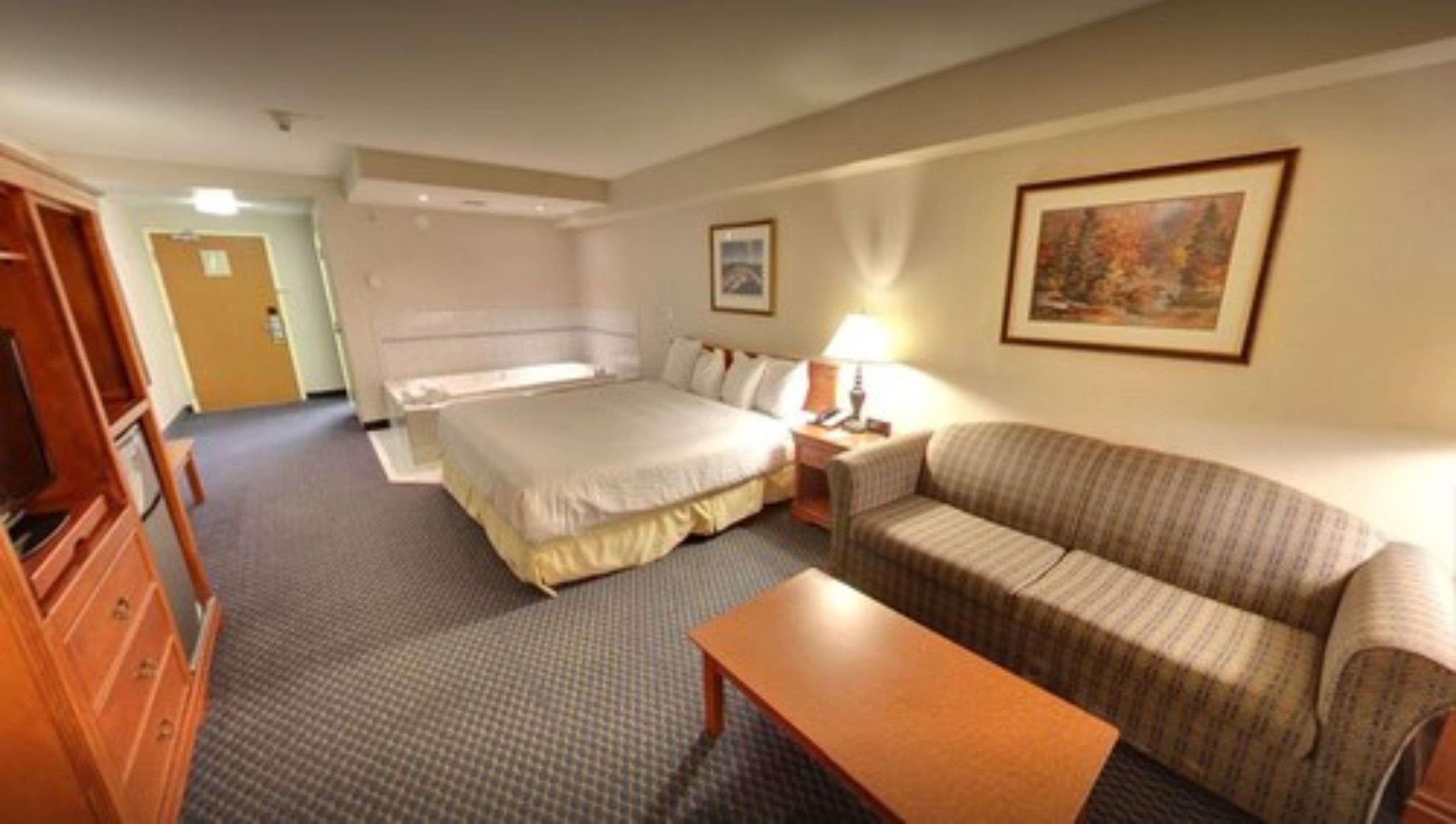 A hotel room with a bed, a sofa, a table, and a painting on the wall.